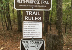 A post at a trailhead has signs indicating what users can use the trail, what the trail rules are, and shows who should yield to who.