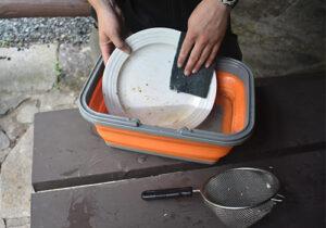 a person washing a dish in a greywater tub